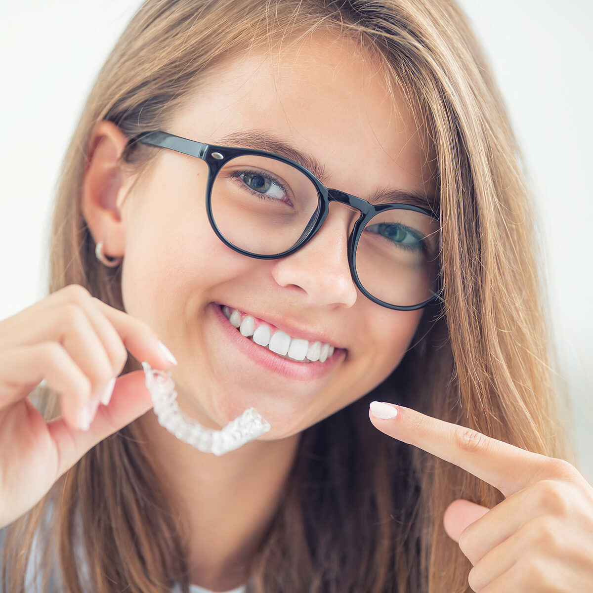 Dental invisible braces or silicone trainer in the hands of a young smiling girl. Orthodontic concept - Invisalign.
